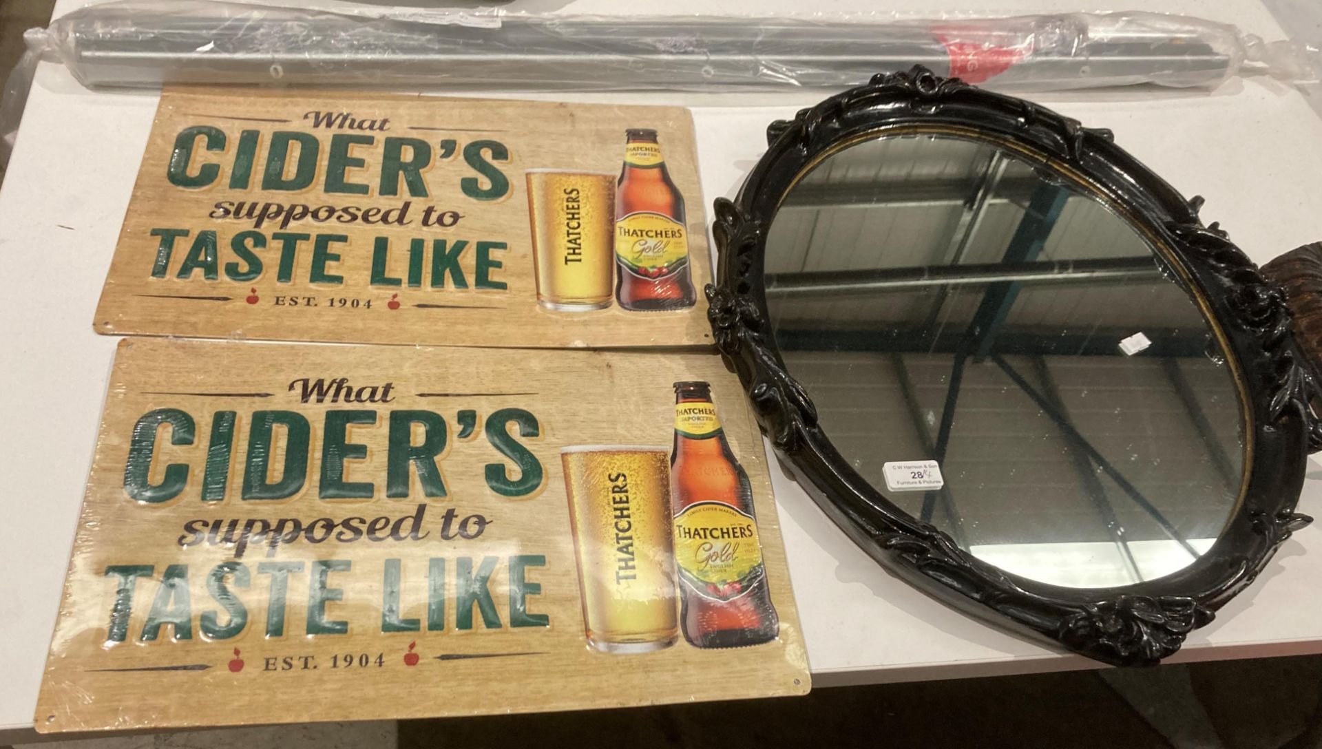 A black painted oval framed wall mirror, 60cm x 45cm, two modern metal wall signs 'Thatchers Cider',