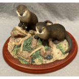 A Border Fine Arts Country Characters 'A1018 Riverdance' otter group on wood plinth, 20cm long.