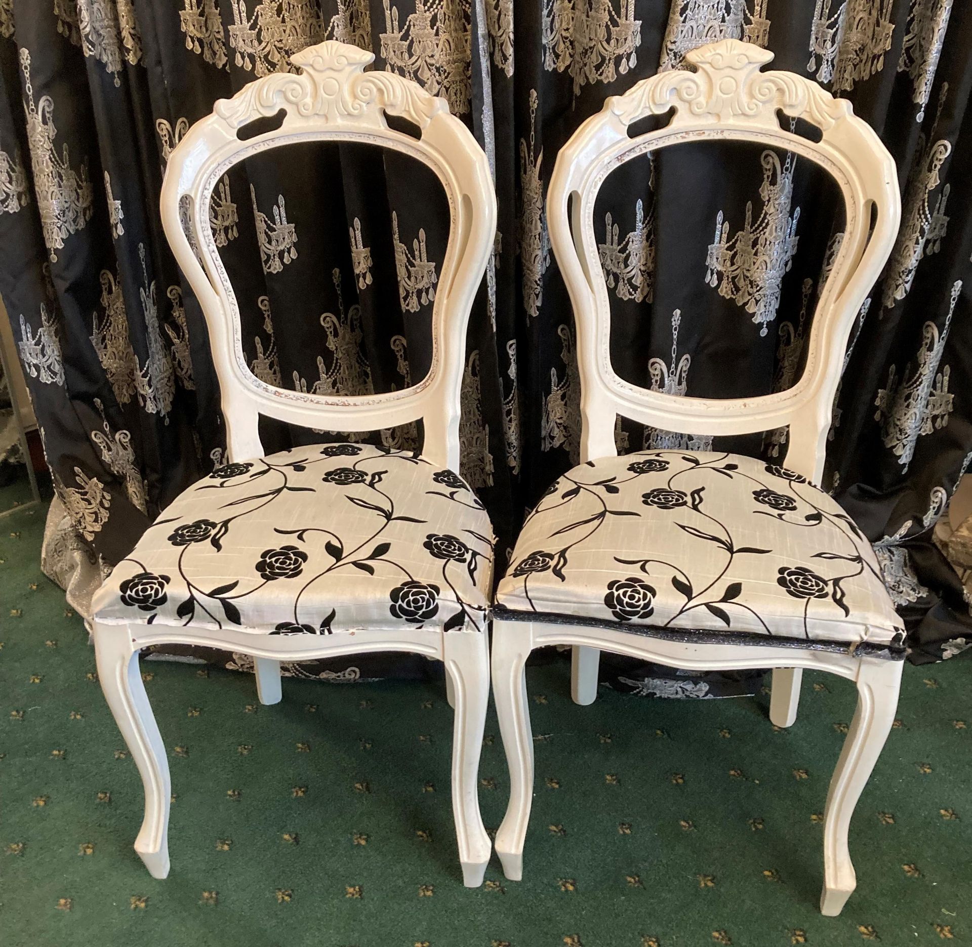 A pair of white painted side chairs with white and black floral fabric seats.