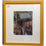 A signed album cover of Bob Dylan 26cm x 20cm in yellow frame complete with a signed note from