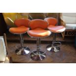 A set of three orange and chrome bar stools,
