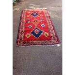 A wool red ground rug with blue and orange central medallion design,