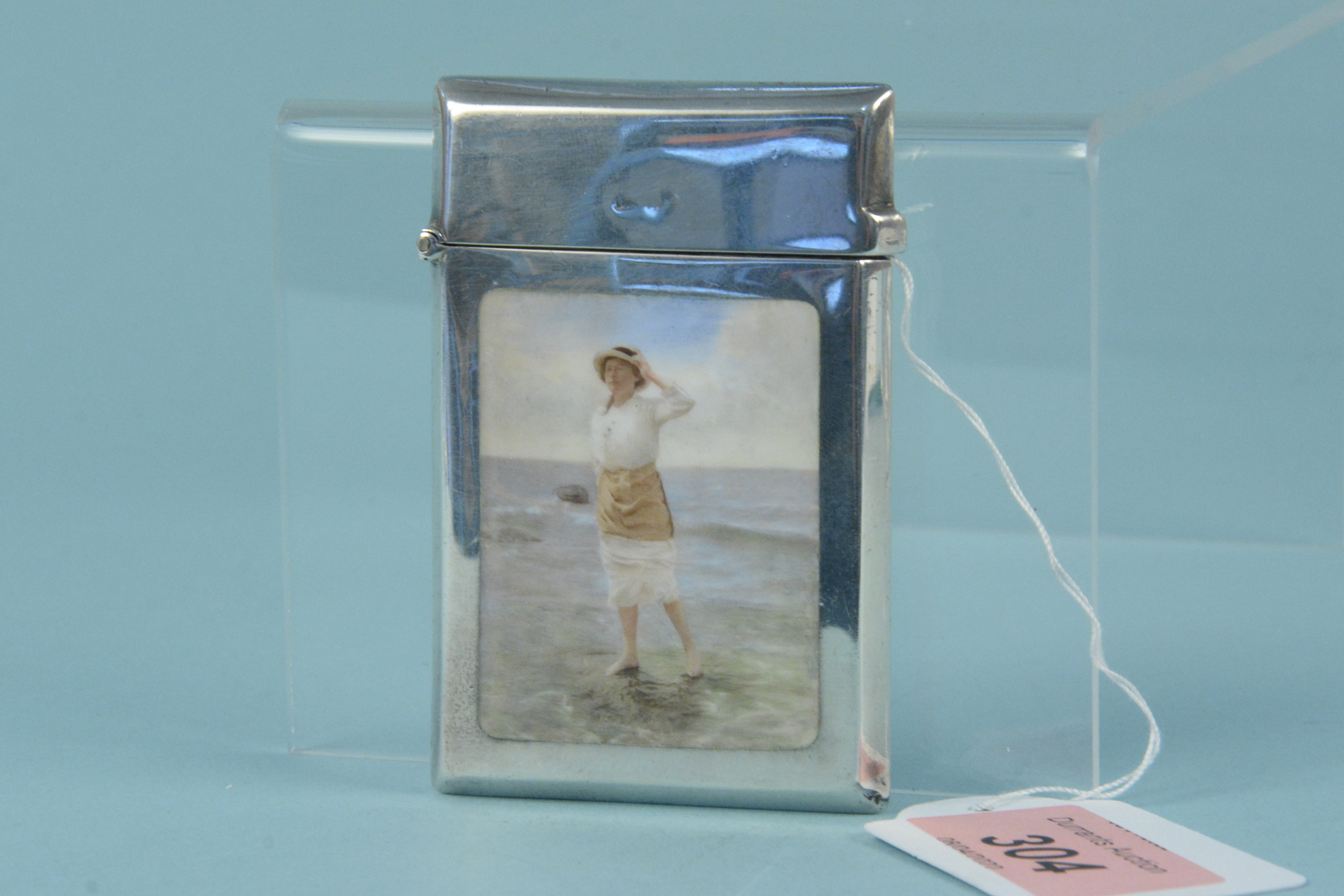 A silver card case with enamelled beach scene to both sides, one side with a lady paddling in water,