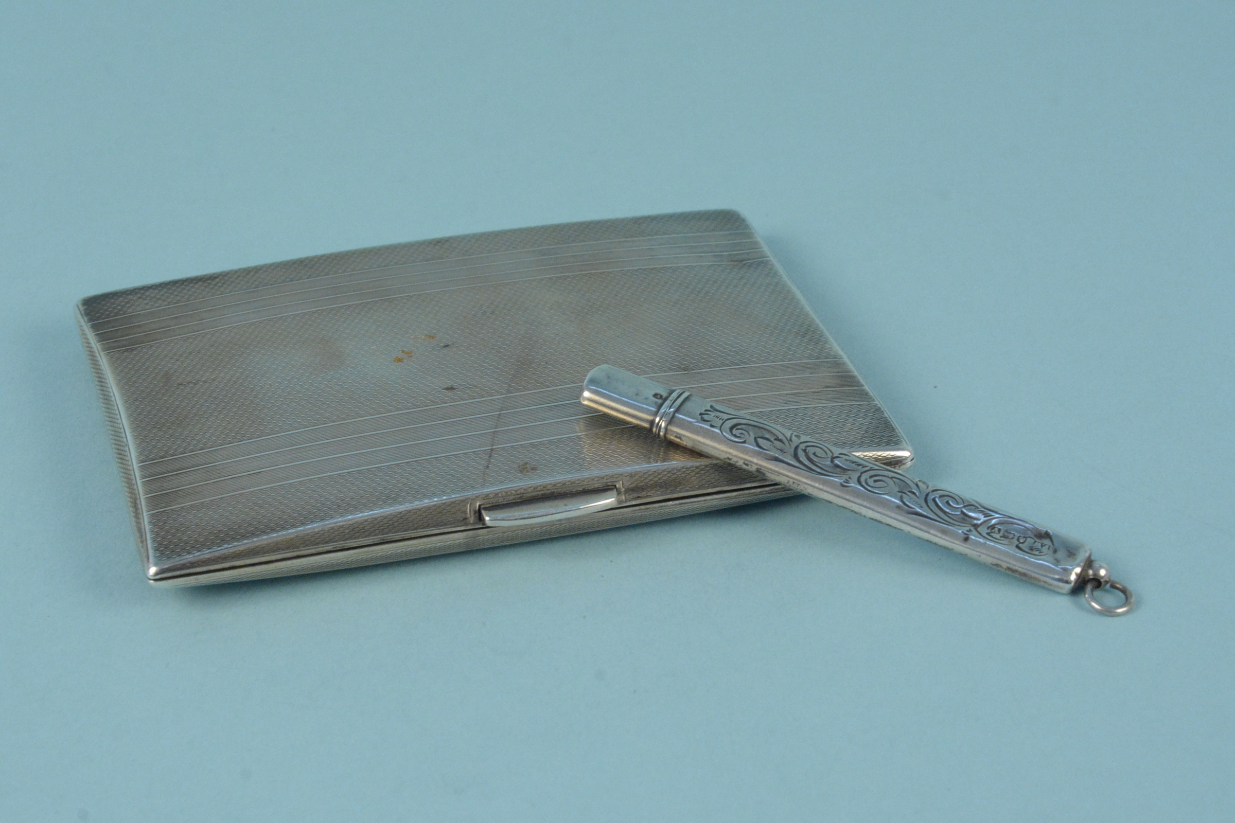 A silver cigarette case with engine turned detail and engraved monogram,