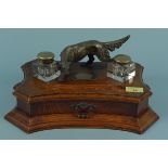 An Edwardian gentleman's desk inkstand in oak with a silver plated red setter mounted to the top