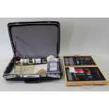A black attaché case with mixed artists materials including a wooden box of pens, crayons, paints,