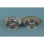 A pair of white metal coasters with turned wooden bases and engraved floral design,