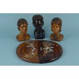 Three carved wooden African heads and a pair of rosewood elliptical wall plaques inlaid with
