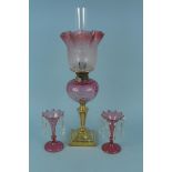 A Victorian brass oil lamp with cranberry glass reservoir and etched cranberry shade plus a pair of