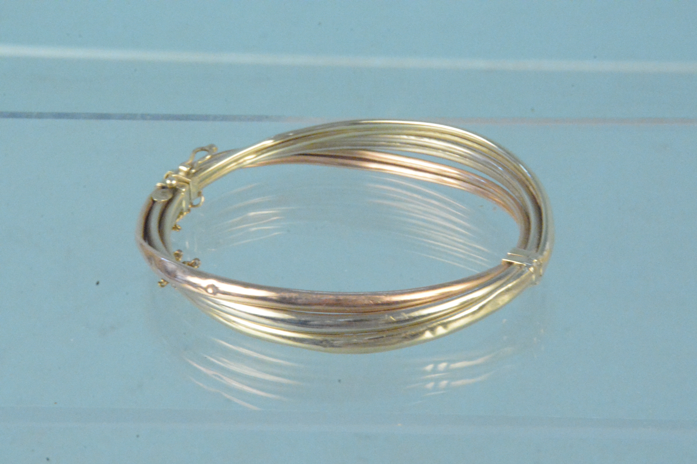 A yellow metal tri-colour bangle, marks rubbed (heavily dented),