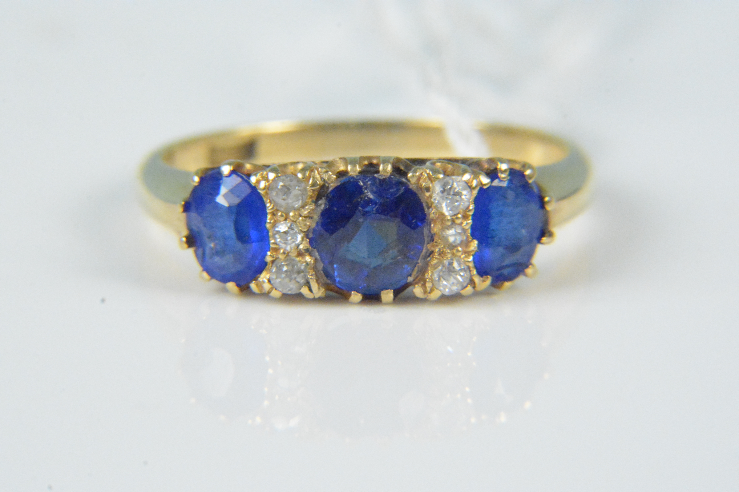 An 18ct gold sapphire and diamond ring, the three claw set sapphires interspaced with small diamond