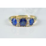 An 18ct gold sapphire and diamond ring, the three claw set sapphires interspaced with small diamond