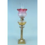 A large size solid brass oil lamp with decorative column and cranberry glass shade,