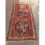 A multi coloured red ground wool rug with tri-central design,