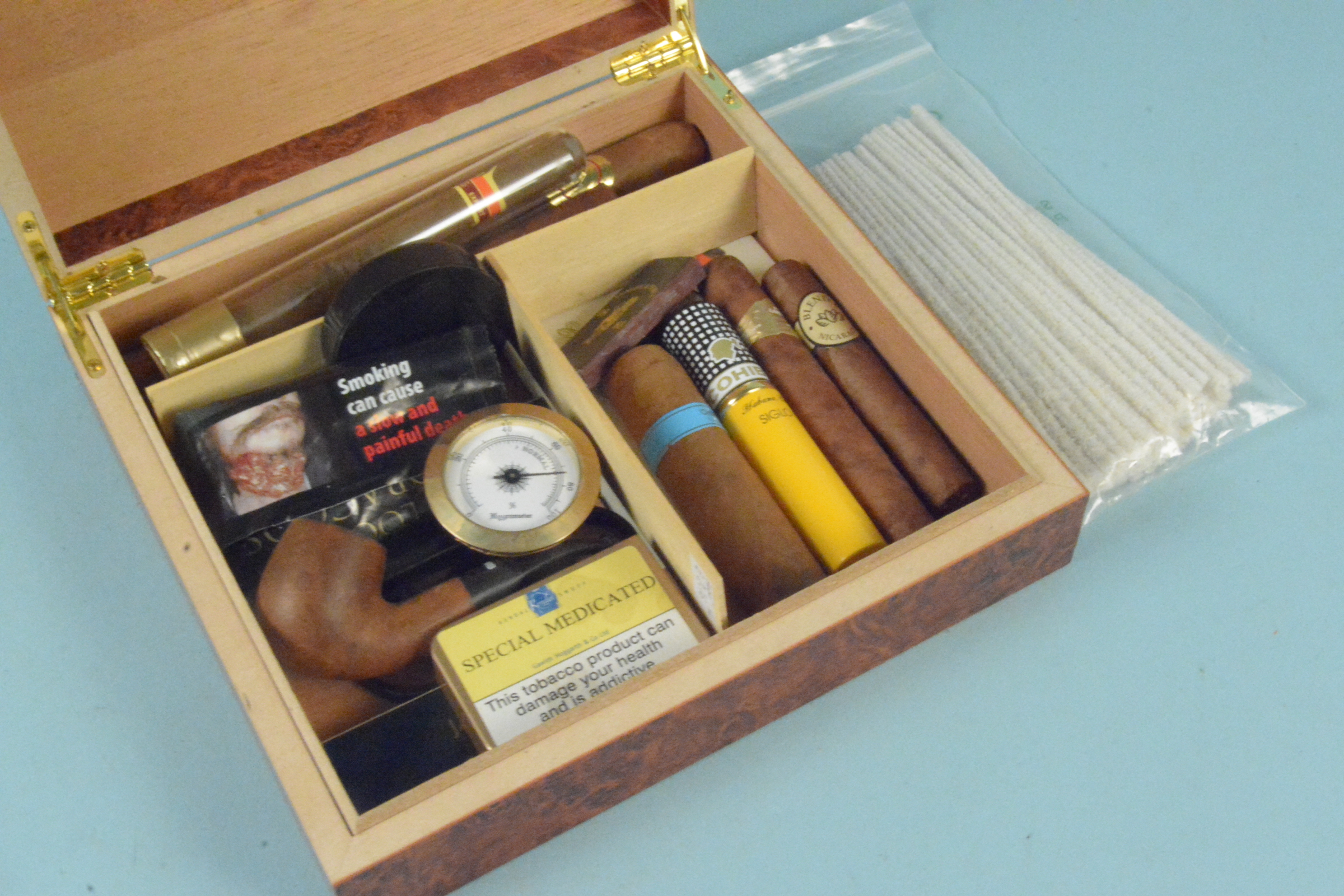 A humidor with cigars, some wrapped, some loose,