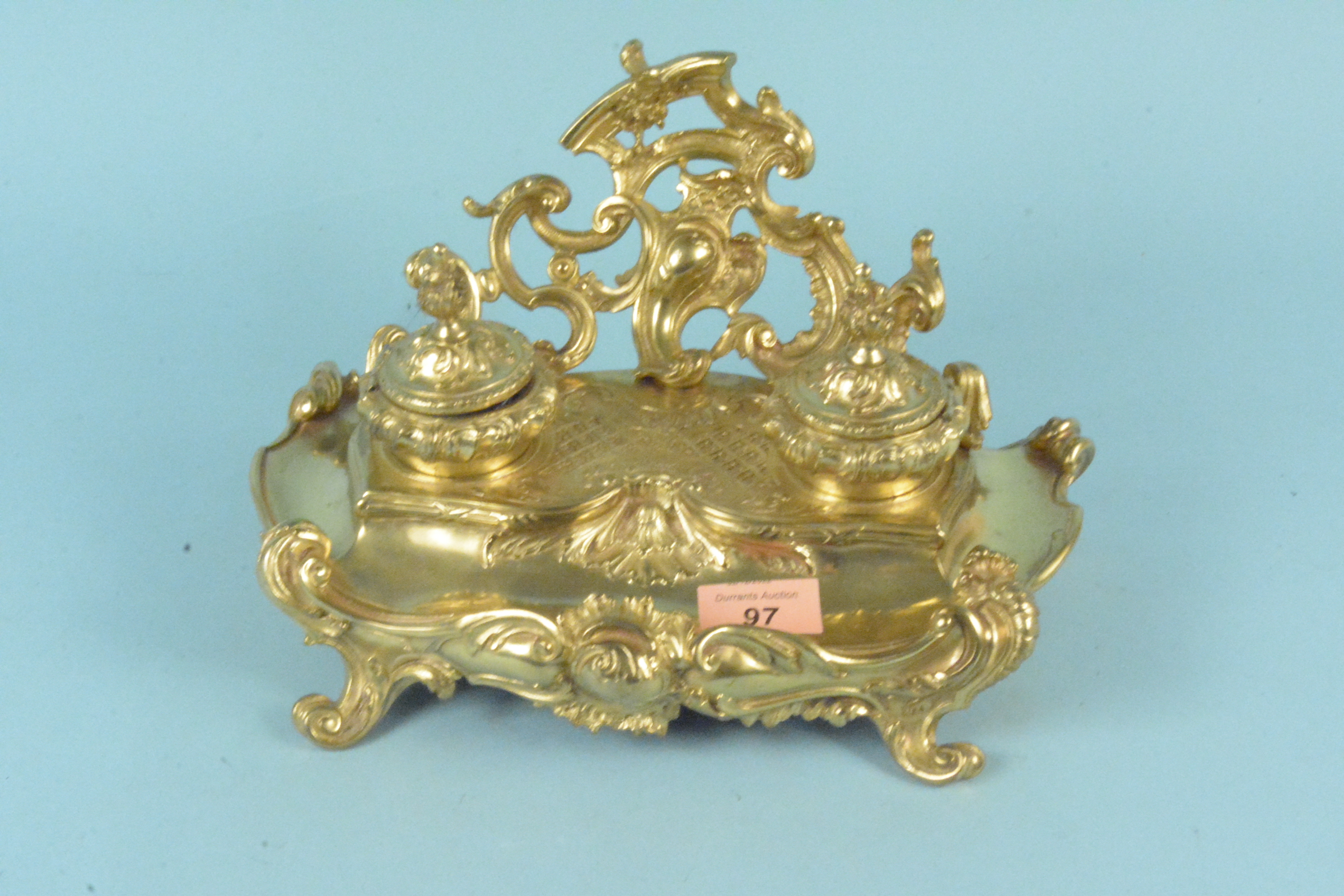 A late 19th Century continental gilt brass inkstand of Rococo design with two lidded inkwells,