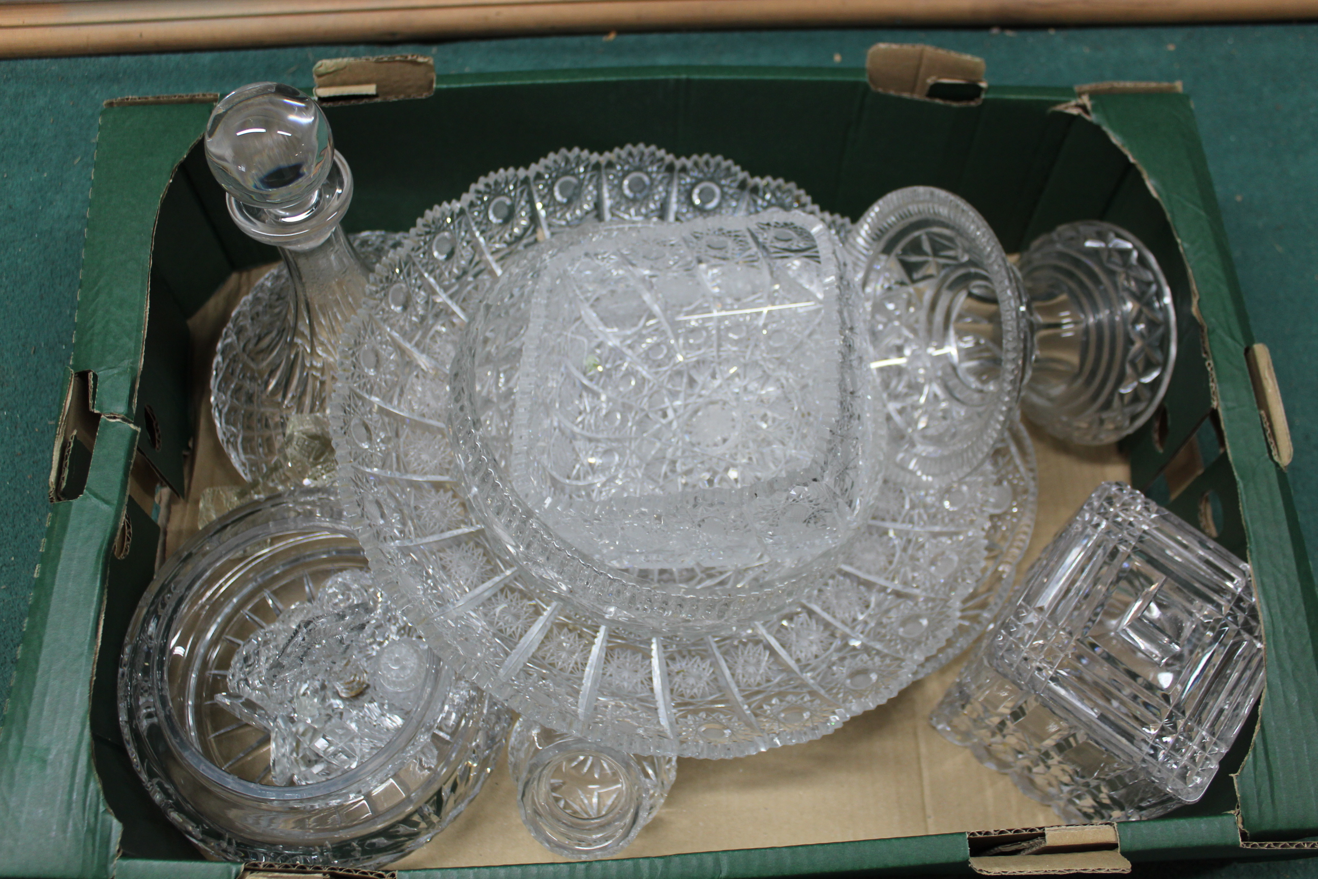 A box of various cut crystal glass items including a large plate, lidded biscuit barrel, cruet,