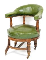 A 19thC oak revolving library chair, upholstered in green leather on turned supports on castors,