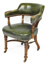 A late Victorian walnut library chair, upholstered in green leather with brass studded borders, on