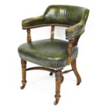 A late Victorian walnut library chair, upholstered in green leather with brass studded borders, on