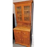 A narrow pine dresser, the top with two glazed doors above a recess, the bottom with two drawers and