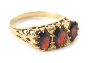 A ladies 9ct gold garnet dress ring, with three claw set faceted cut stones on a pierced shank decor