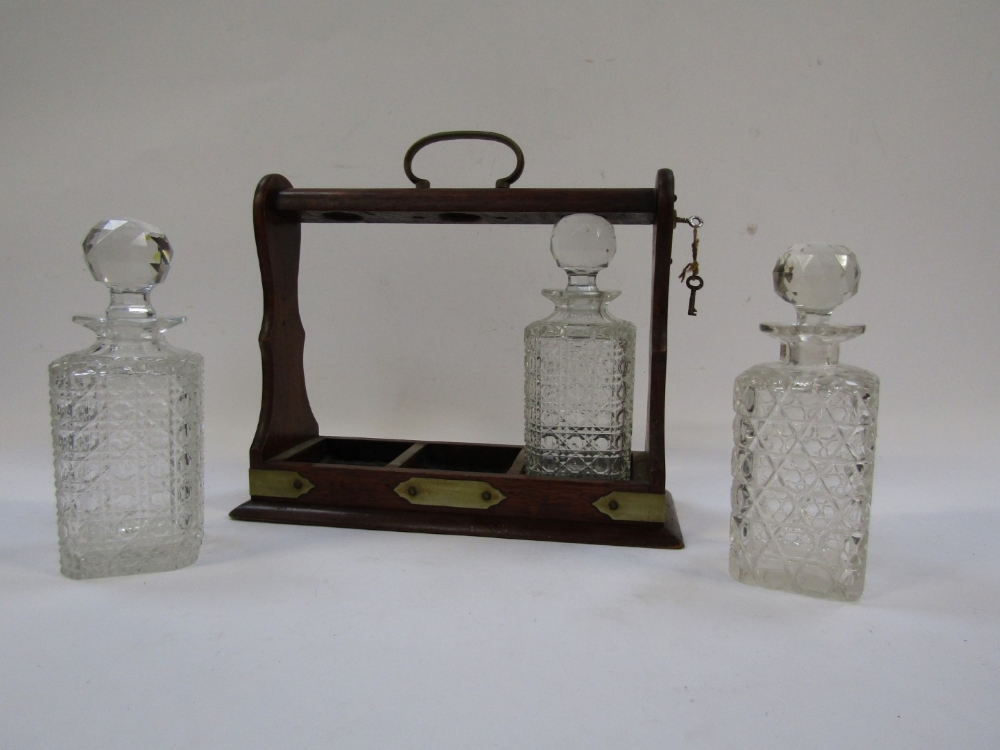 An oak Tantalus, with brass bound detailing, enclosing three cut glass decanters, each with stopper, - Image 2 of 4