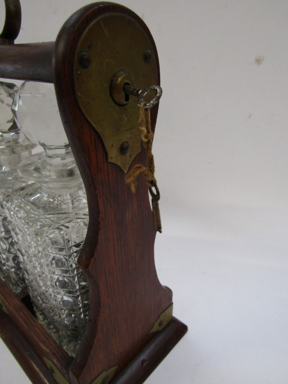 An oak Tantalus, with brass bound detailing, enclosing three cut glass decanters, each with stopper, - Image 4 of 4