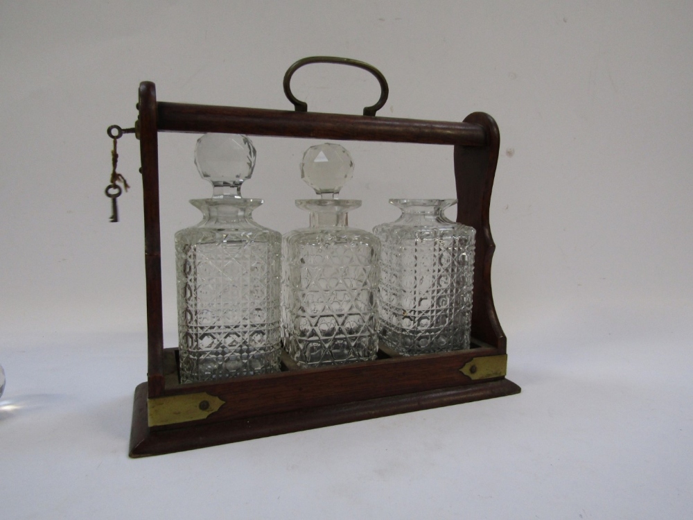 An oak Tantalus, with brass bound detailing, enclosing three cut glass decanters, each with stopper, - Image 3 of 4