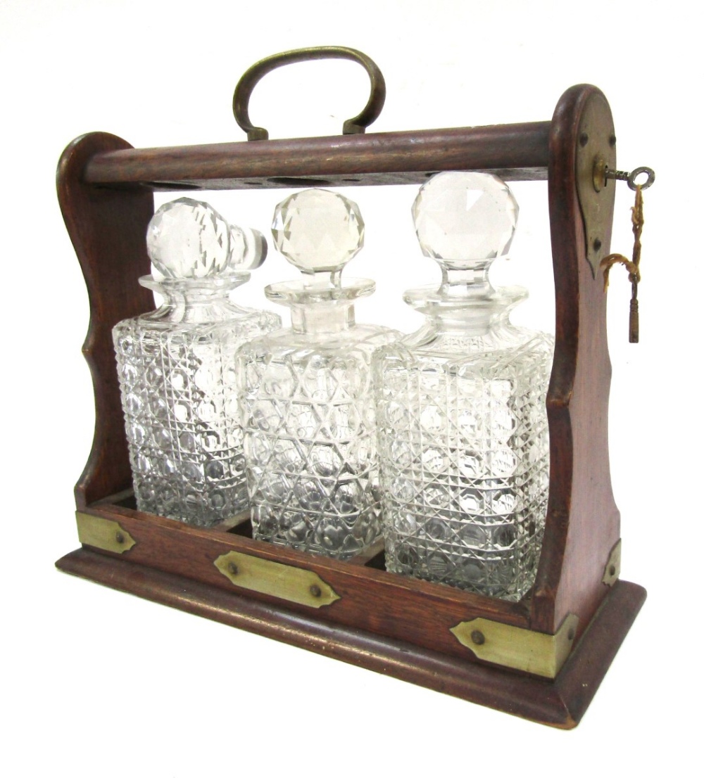 An oak Tantalus, with brass bound detailing, enclosing three cut glass decanters, each with stopper,