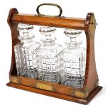 An early 20thC oak cased tantalus, with plated mounts, worn, containing three cut glass decanters an