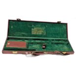 A maroon leather gun case, with brass clasps, with a fitted interior, 82cm wide.