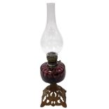 An early 20thC cast iron and brass oil lamp, with an amethyst glass reservoir, glass chimney, raised