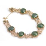 A fancy link yellow metal bracelet, broken by polished oval green stones, with an arrangement of flo