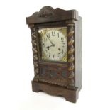 An early 20thC oak mantel clock, the arched top with fleur de lis panel, on barley twist columns wit