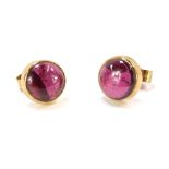 A pair of stud earrings, each with a cabochon purple coloured stone, in rub over setting, with a sti