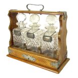 A 19thC oak tantalus, the oak case with buckle supports and three cut glass decanters, each with sil