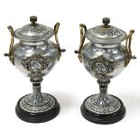 A pair of late 19thC French white metal urns and covers, with brass handles, of baluster form, embos