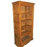 A Victorian style mango wood open bookcase, the outswept pediment over a front carved with laurel le