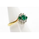 An 18ct gold emerald and diamond cross over ring, with three emeralds, one round brilliant cut and