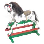 A dapple grey rocking horse, with horse hair mane, leather saddle, metal stirrups on a green and red