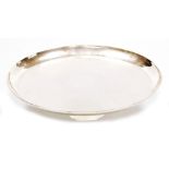 A George V circular silver tray, of plain form with an everted border, raised on three feet, London