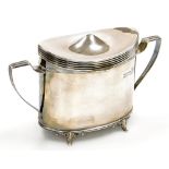 An Edwardian silver tea caddy, of oval form, with two angular handles, raised on four scroll cast fe