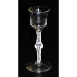 An 18thC wine glass, with dimpled thistle shaped bowl and knopped opaque lace twisted stem, on a con