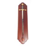 A replica Excalibur presentation sword, with gold coloured handles, on a presentation mahogany shiel