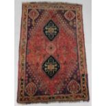 A Persian rug, with two lozenge shaped medallions, on a red ground with purple geometric spandrels,
