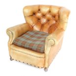 A vintage tan leather button back armchair, with a loose tartan seat, raised on castors,
