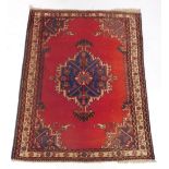 A Persian rug, with a central shaped medallion in blue, on a red ground, with purple spandrels withi