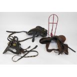 A group of saddles and saddle stands, comprising a plain brown leather saddle on red metal stand, an