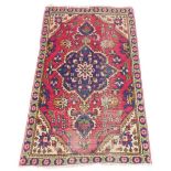 A Persian rug, with a central medallion in blue, surrounded by a meandering design of flowers, on a